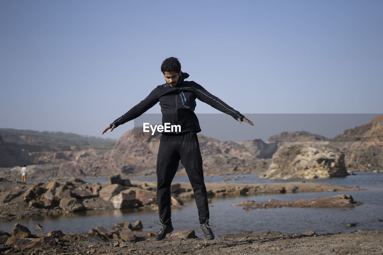 Young athletic man doing burpee near a lake surrounded with mountains early in the morning.