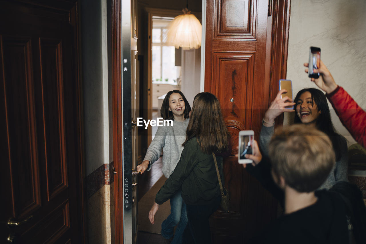 Happy friends photographing girls while standing at doorway