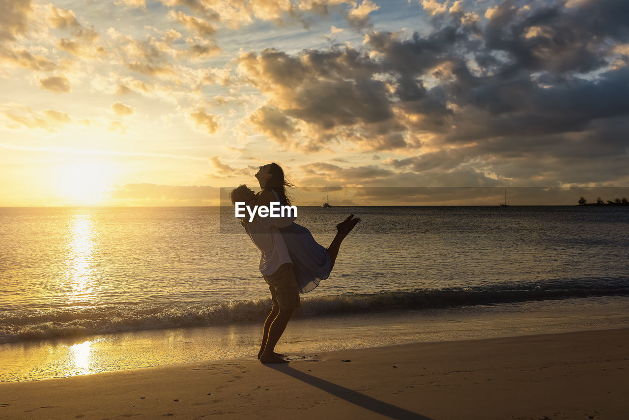 rear view of woman standing at beach against sky during sunset