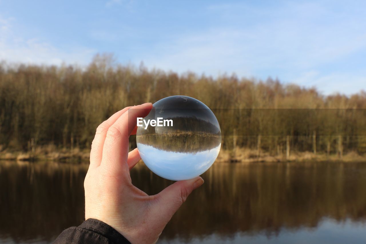 Cropped hand holding crystal ball by lake