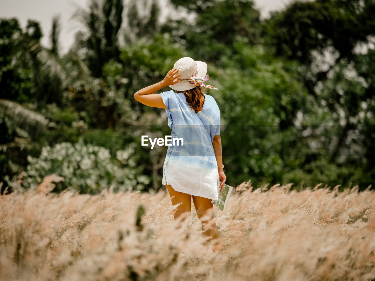 Woman wearing hat while standing on field against trees