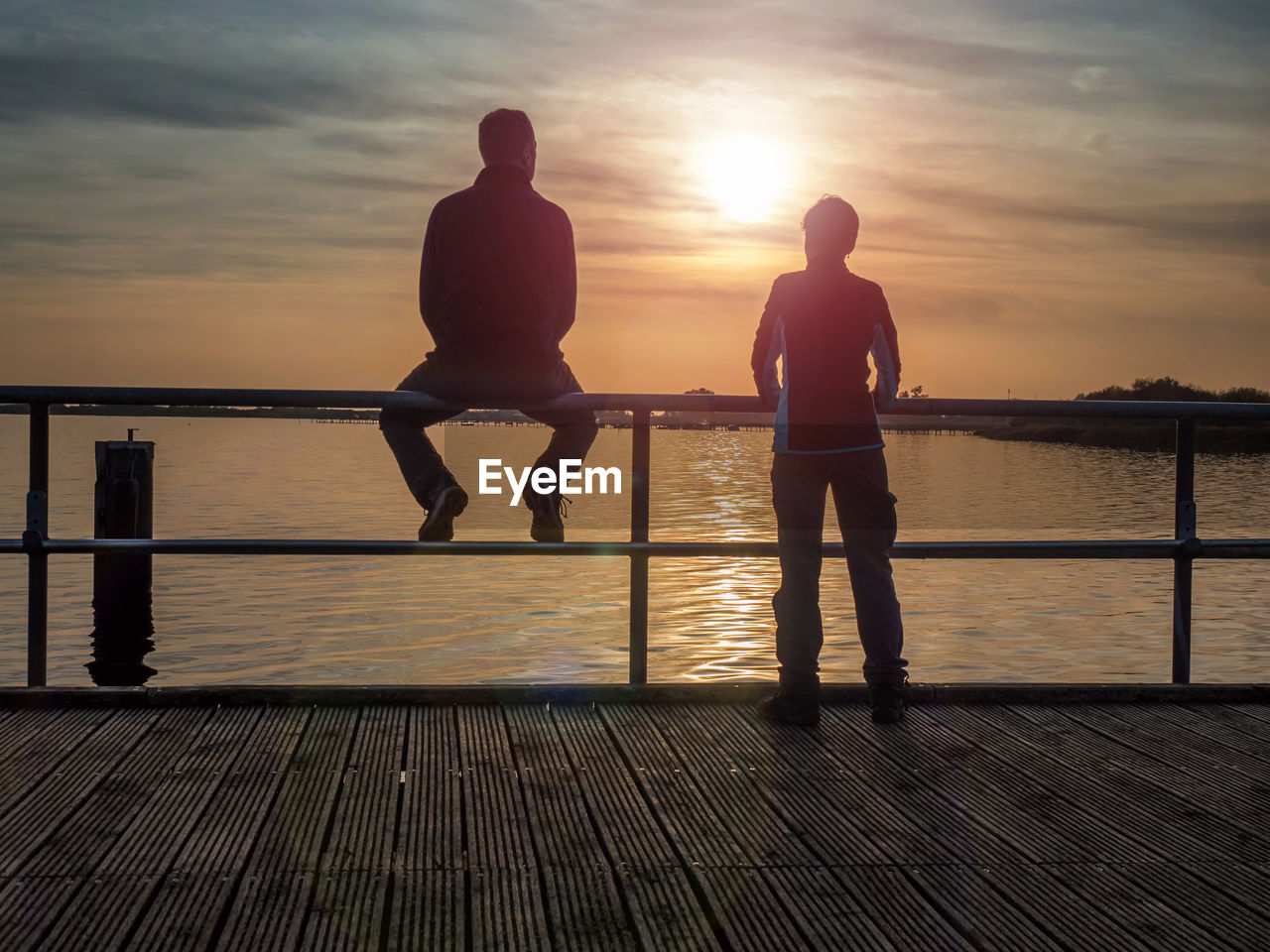 Couple of tourists. a woman leans over the railing and looks at the sunset over the sea. sea bridge