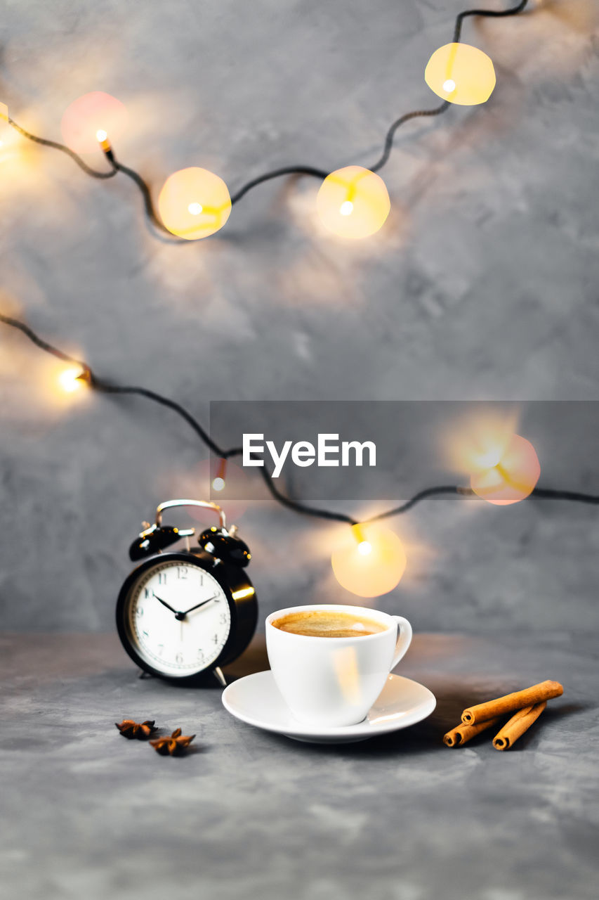 Christmas composition with cup of coffee surrounded by cinnamon, lights and cloves on gray table.