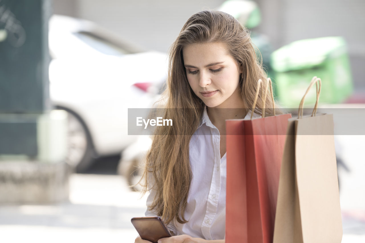 YOUNG WOMAN HOLDING SMART PHONE WHILE USING LAPTOP IN MOBILE