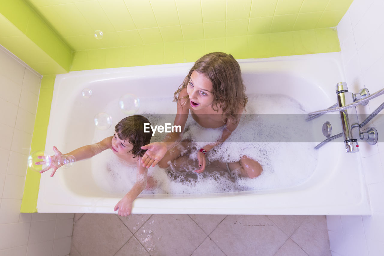 High angle view of happy siblings playing in bathtub