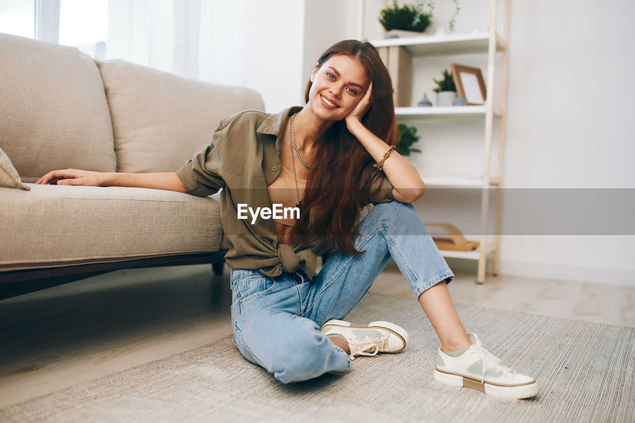 full length of young woman sitting on sofa at home