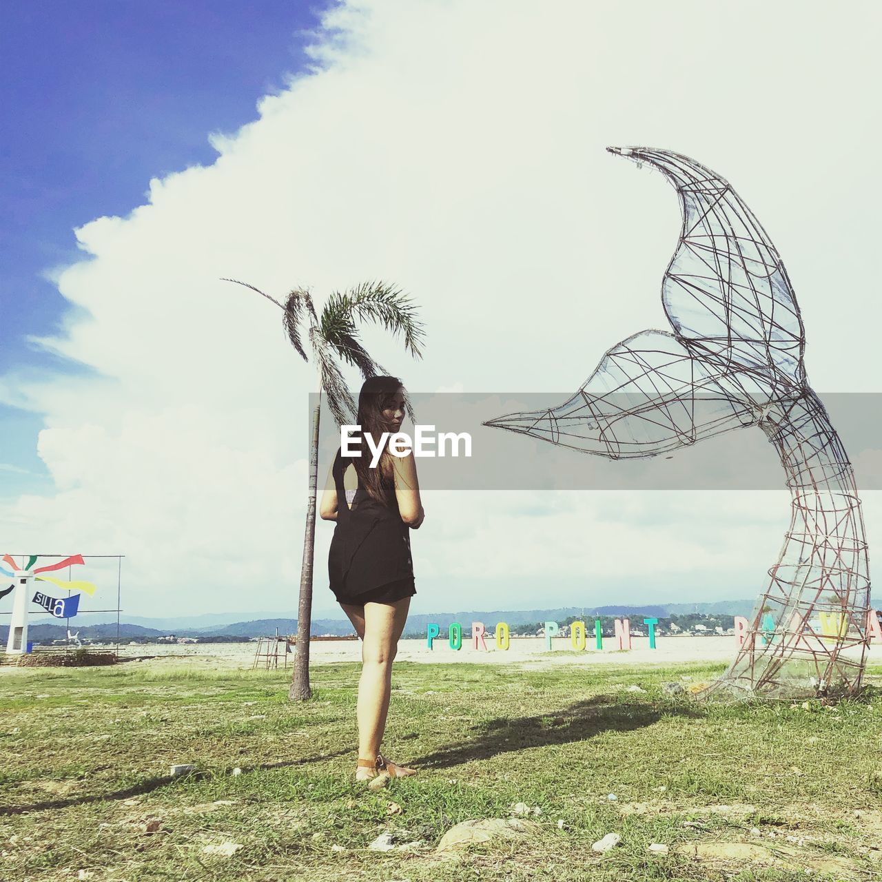 FULL LENGTH OF YOUNG WOMAN STANDING AGAINST SKY