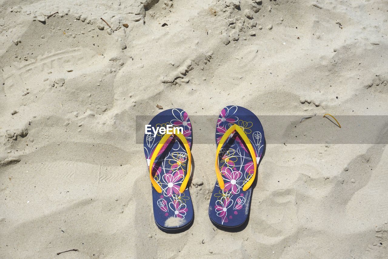 High angle view of flip-flops at sandy beach on sunny day