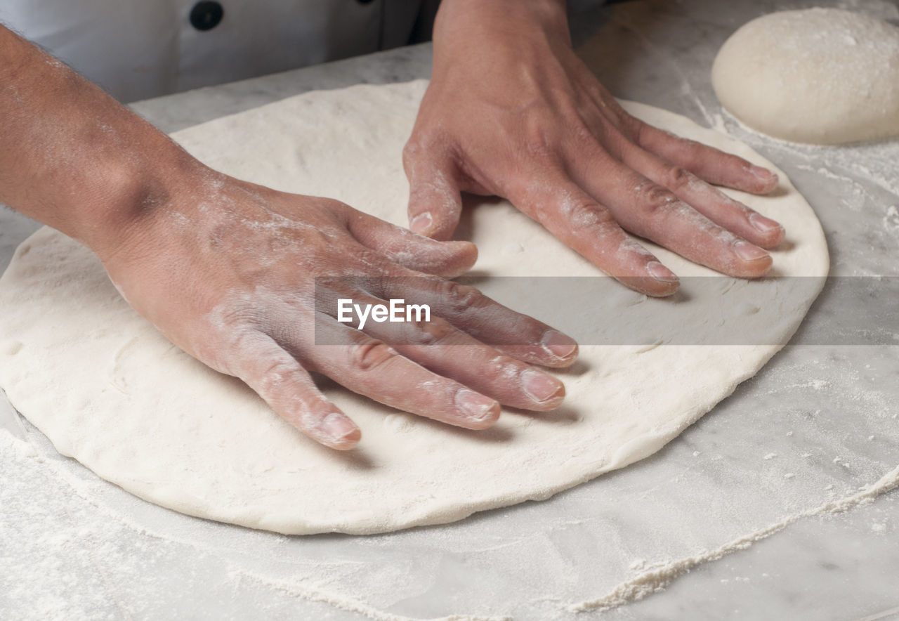 Cropped hands of chef kneading dough on table in commercial kitchen