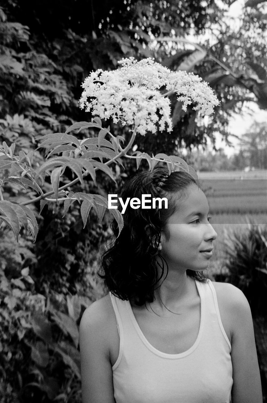 Young woman looking away while standing by plants in yard