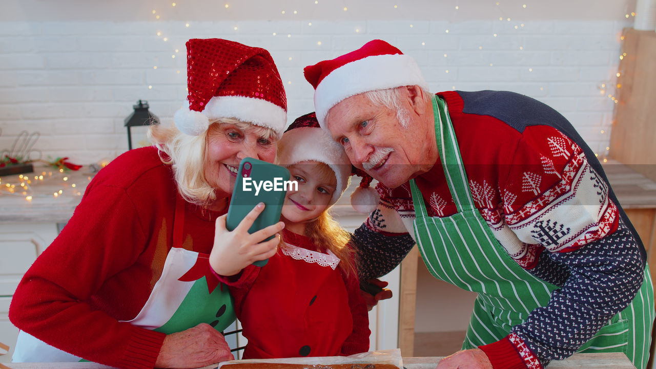 Cheerful grandparents and granddaughter talking on video call at kitchen
