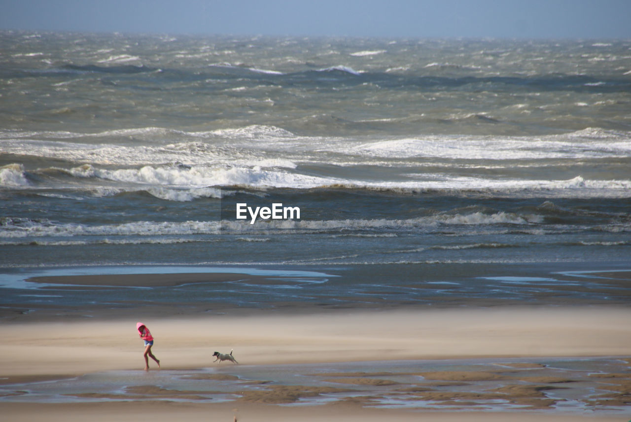 Full length of girl running with dog on beach by sea against sky