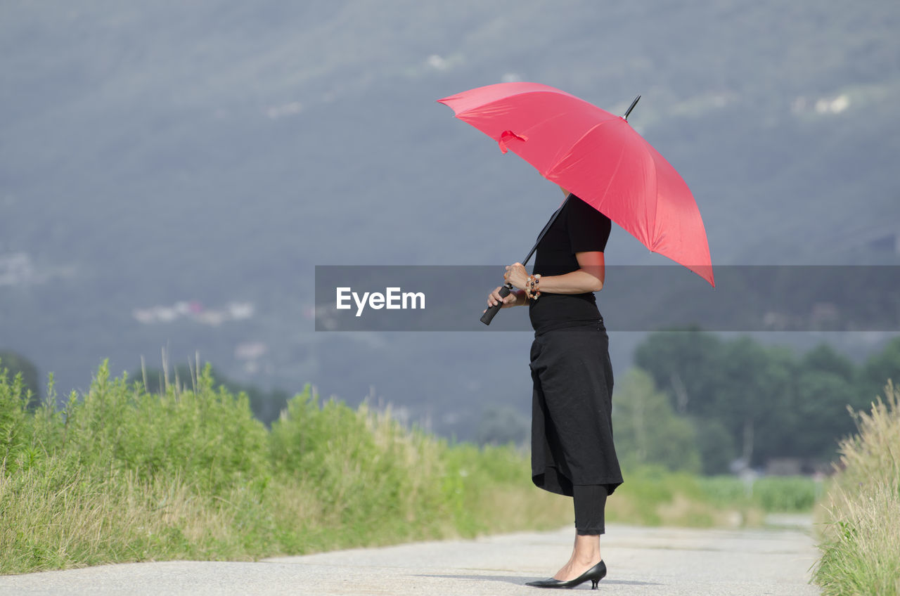 Side view of woman holding umbrella while standing on road