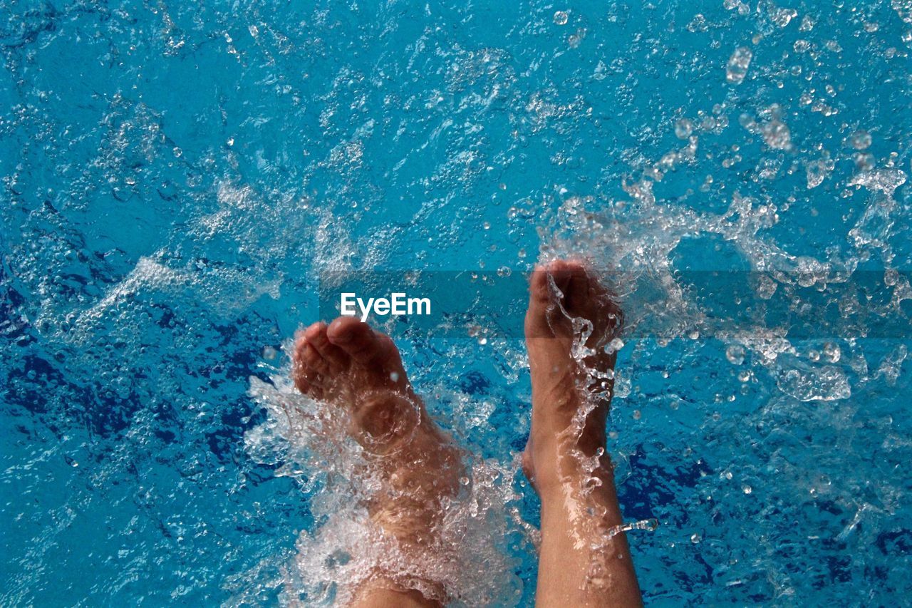 Low section of woman splashing water in swimming pool