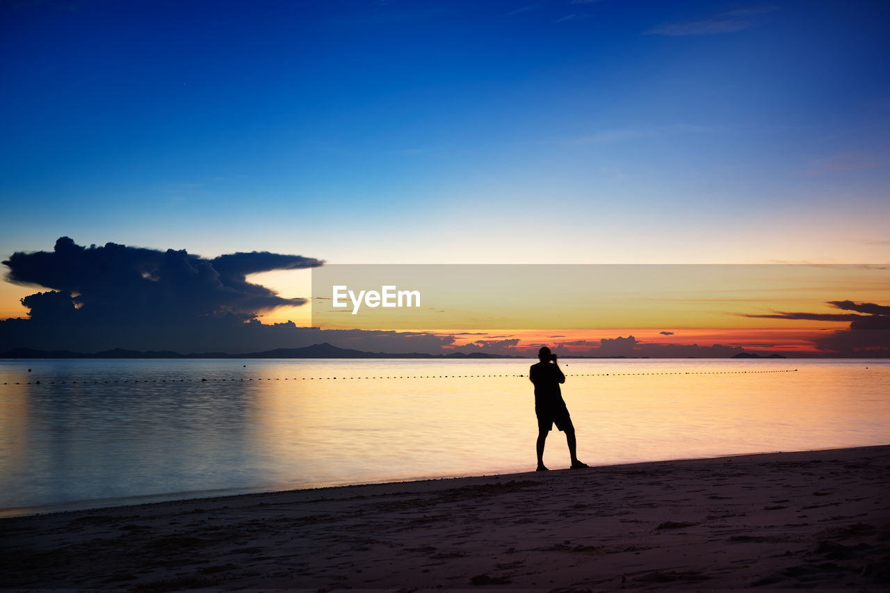 SILHOUETTE MAN STANDING ON BEACH DURING SUNSET