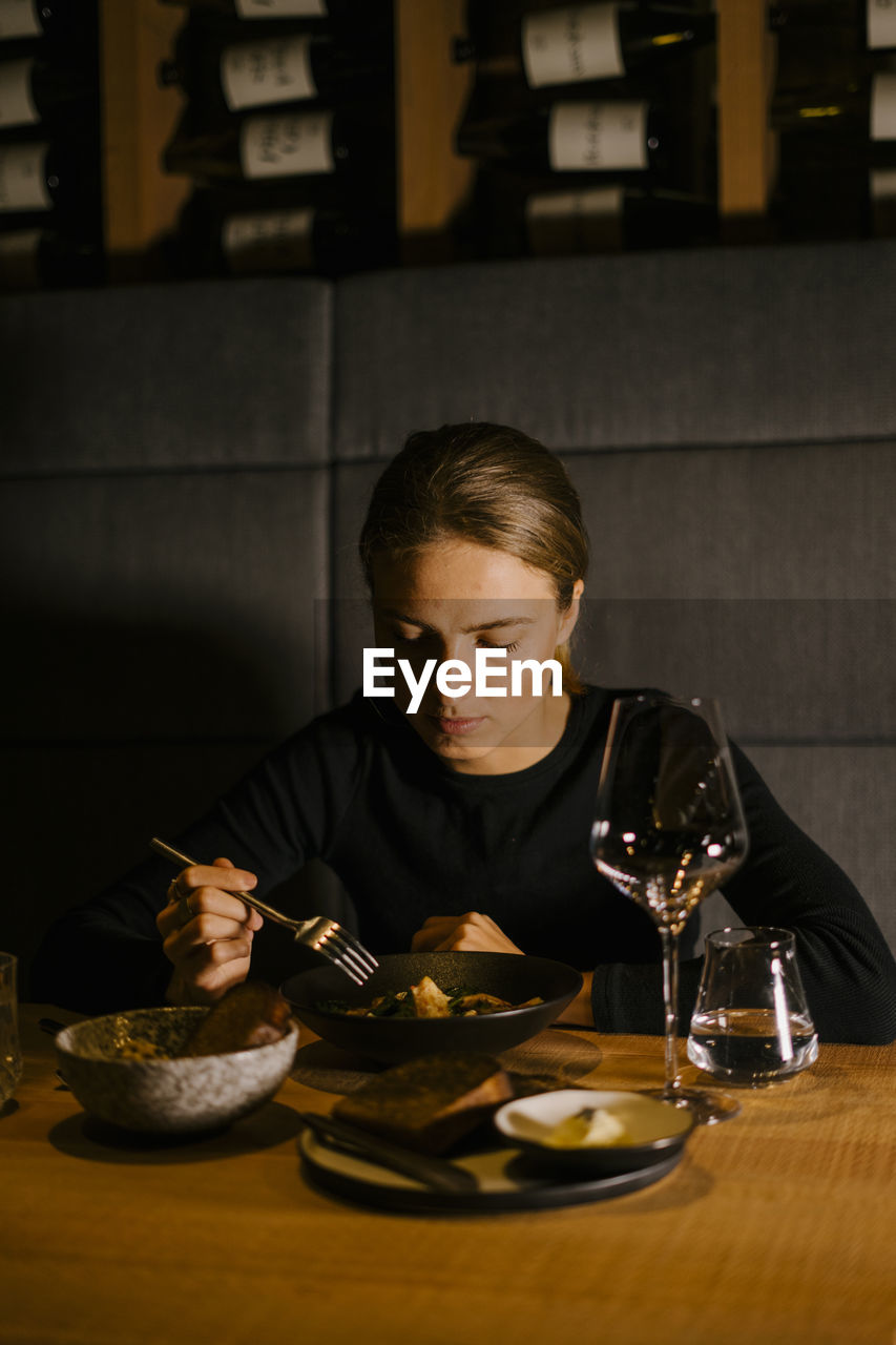 Young woman eating meal at dining table in restaurant