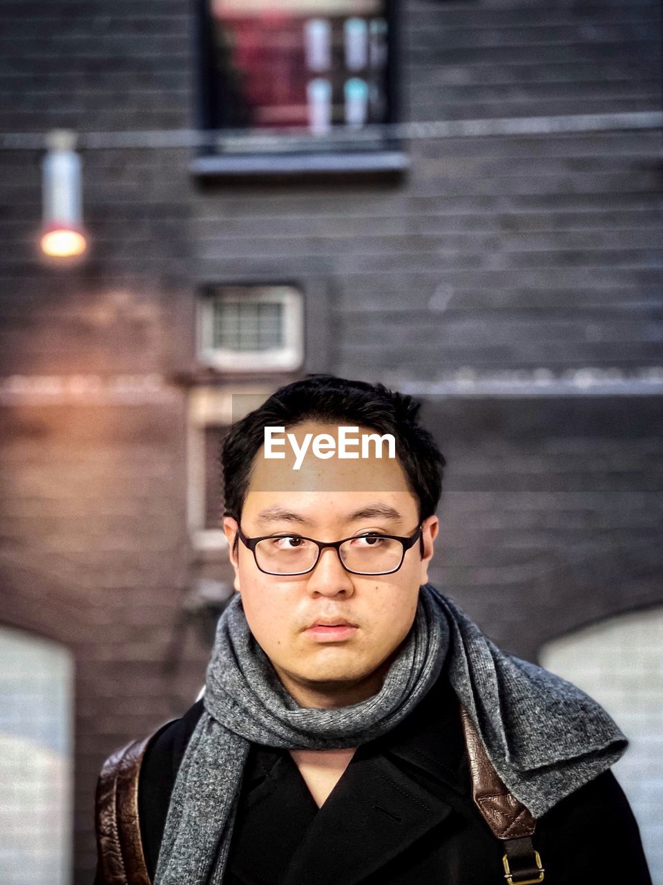 Portrait of young man standing against building exterior in city.