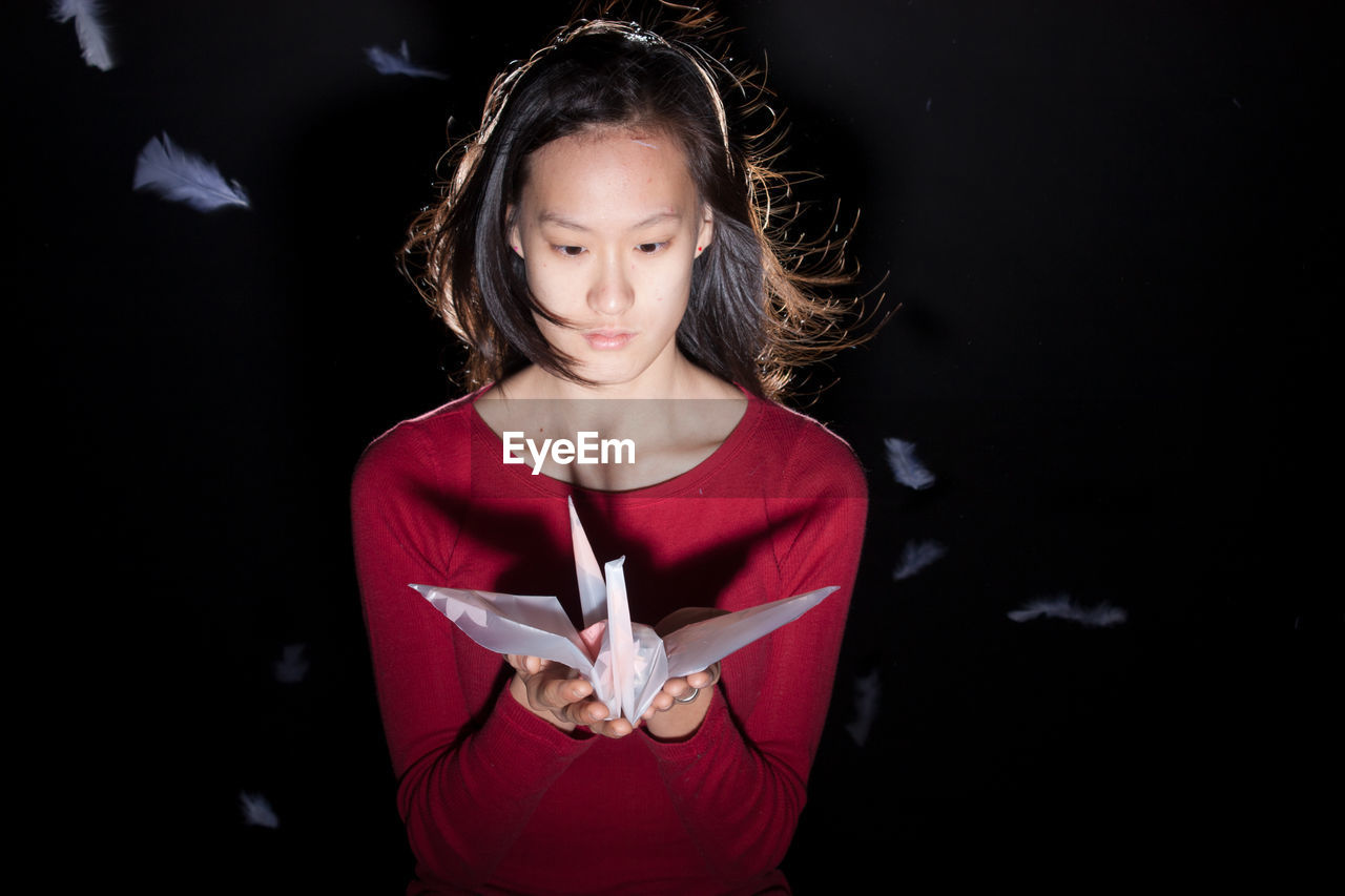 Young woman holding origami standing against black background