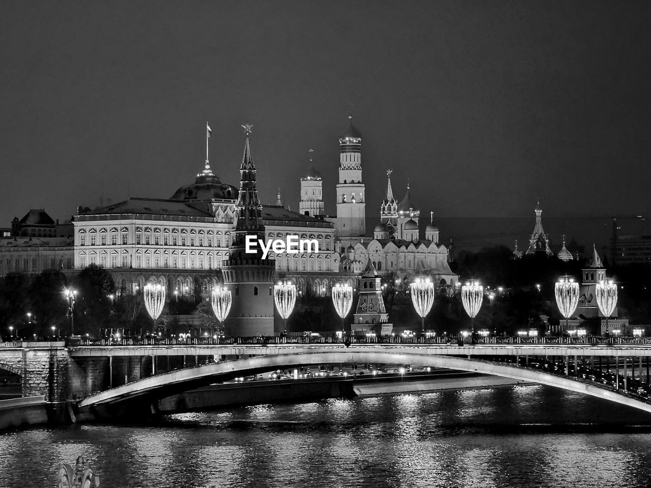 Illuminated bridge over river by buildings against sky at night