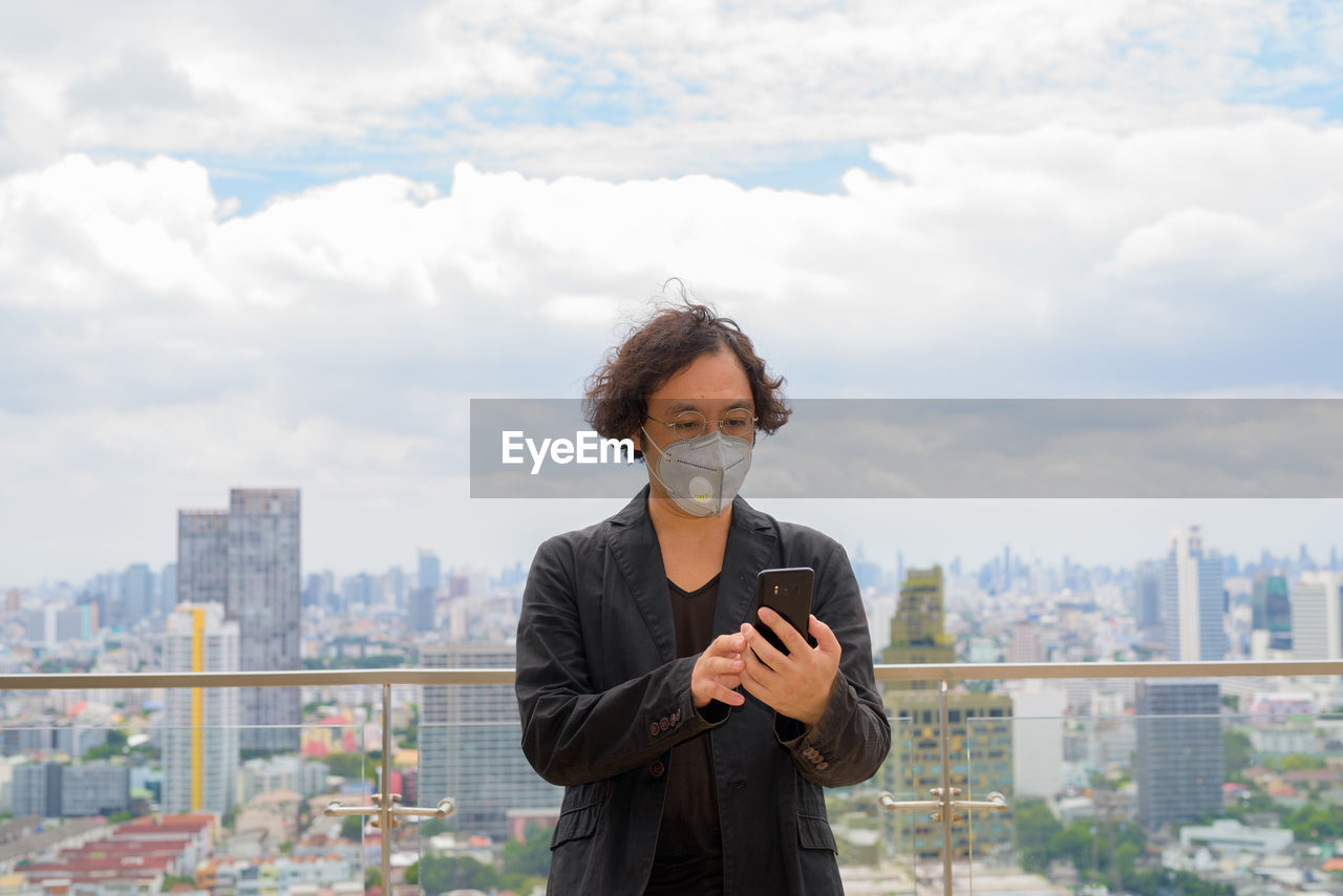 PORTRAIT OF WOMAN STANDING AGAINST CITYSCAPE