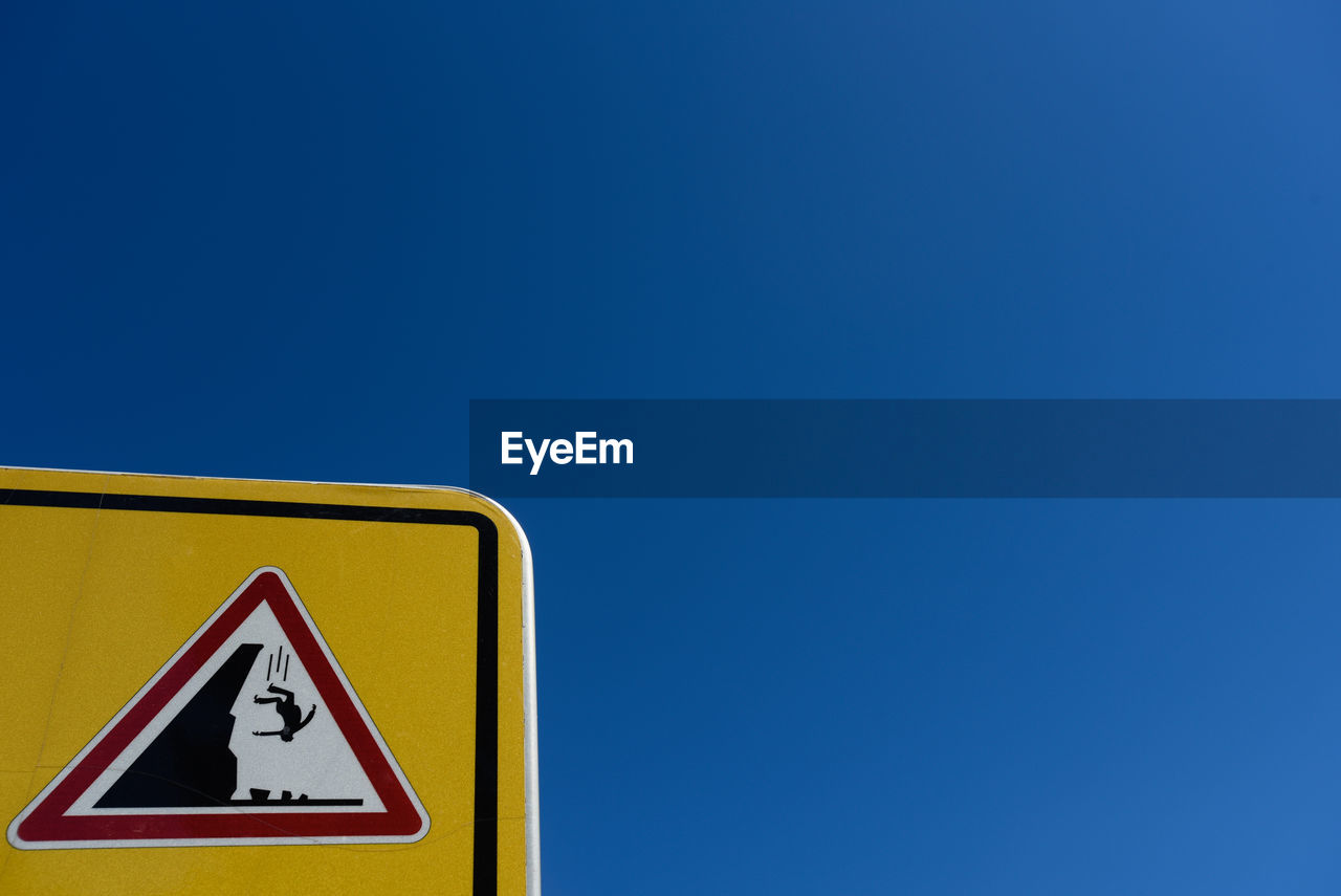 Low angle view of road sign against clear blue sky