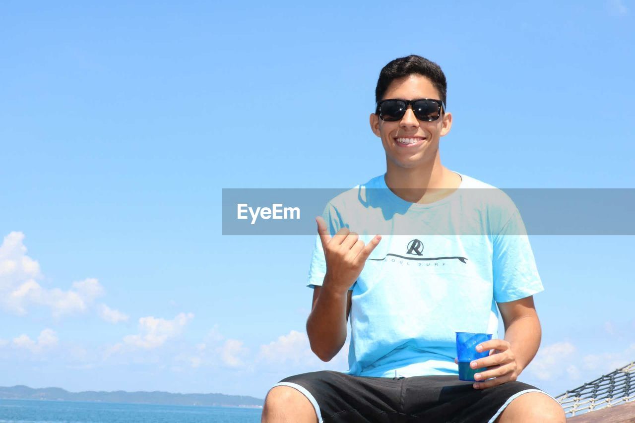 Portrait of smiling young man sitting against blue sky