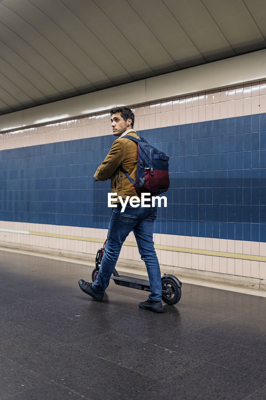 Man in stylish outfit walking with electric scooter in the underground