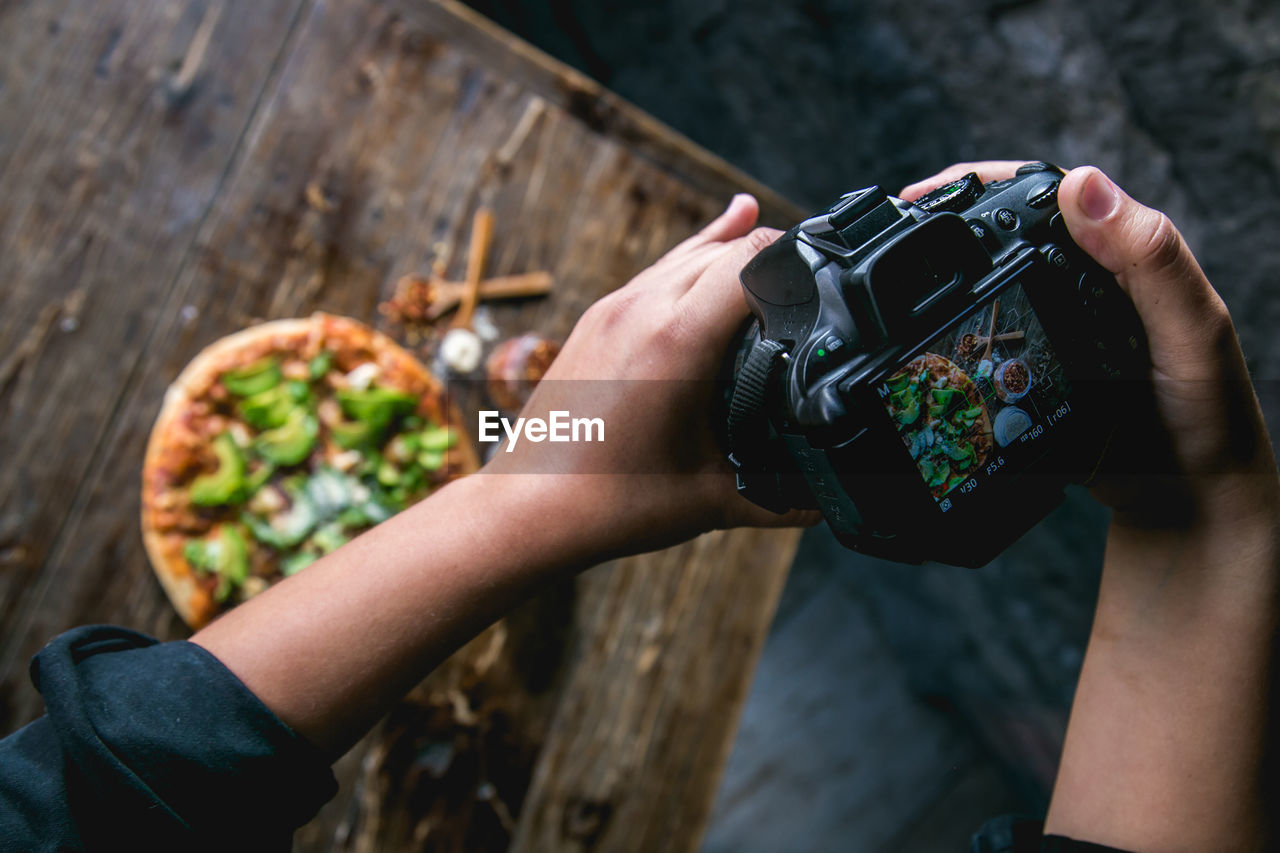 Cropped hands photographing pizza using camera