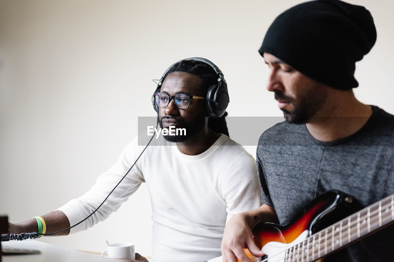 Man playing guitar while friend listening through headphones