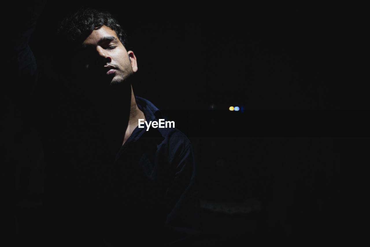 Young man with eyes closed standing against black background