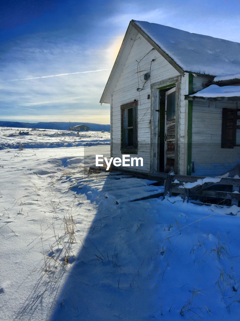 House by snowy field against sky during sunny day