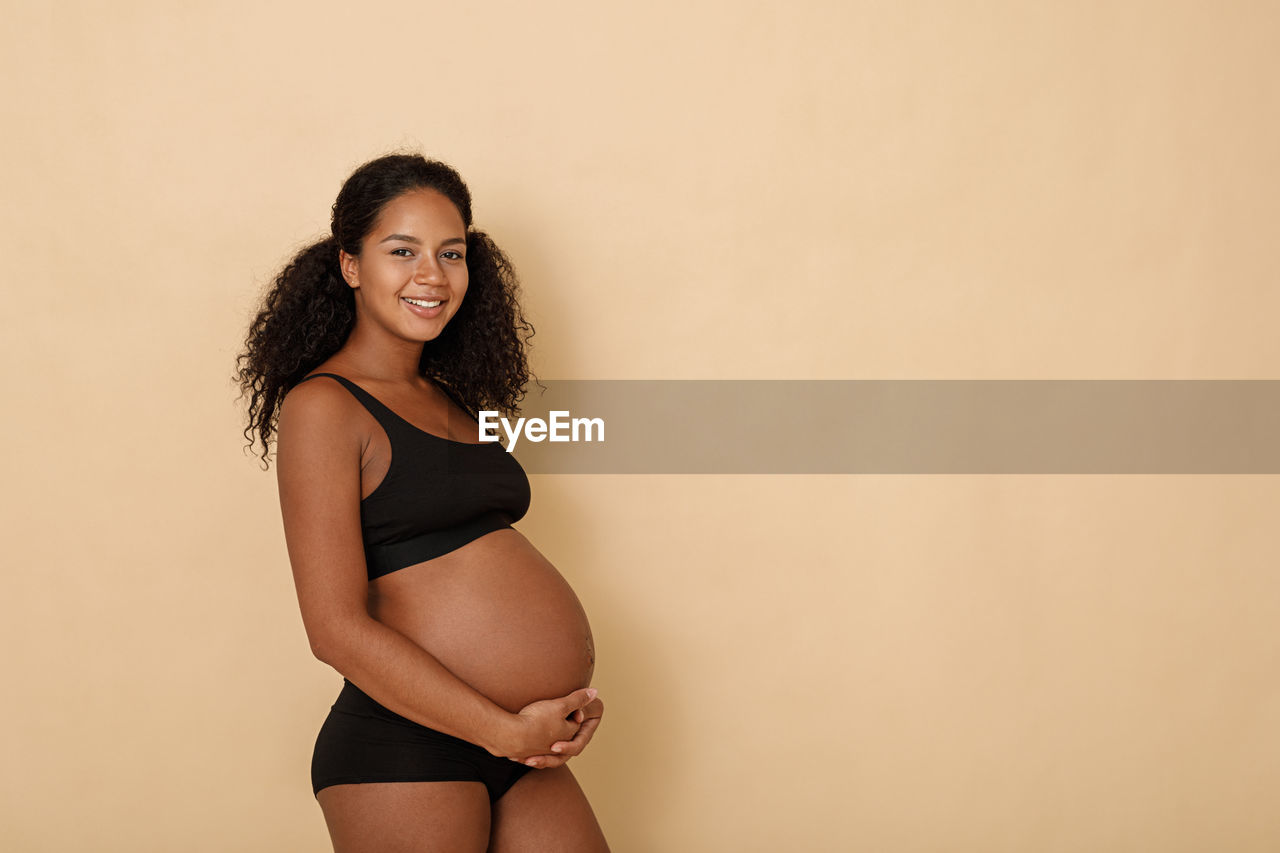 Portrait of smiling pregnant woman standing by wall