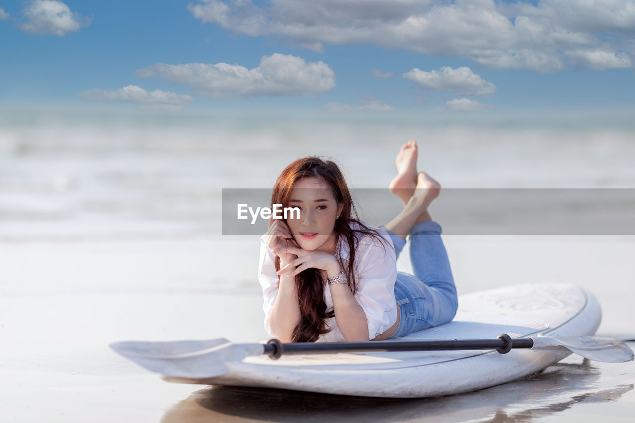 portrait of young woman with arms raised standing at beach