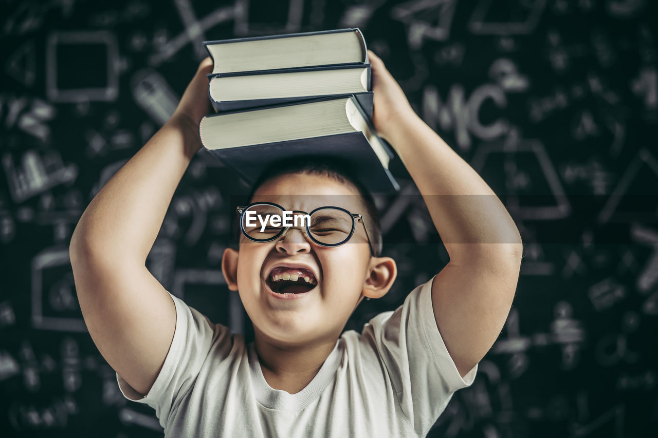 PORTRAIT OF BOY HOLDING BOOK AT CAMERA