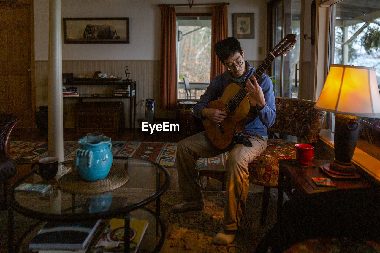 Portrait of a man playing guitar by himself in an eclectic home