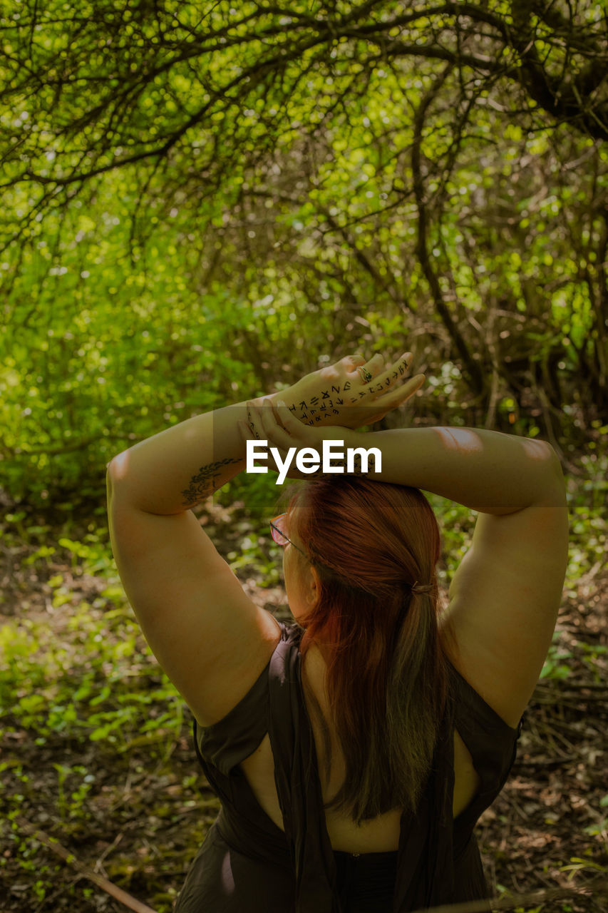 rear view of woman with arms raised against tree