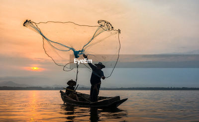 Fisherman throwing net in sea during sunset