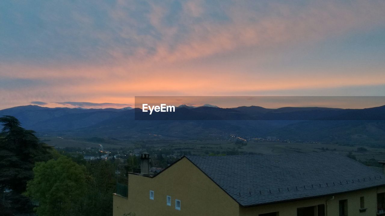 SCENIC VIEW OF HOUSES AND MOUNTAINS AGAINST SKY DURING SUNSET