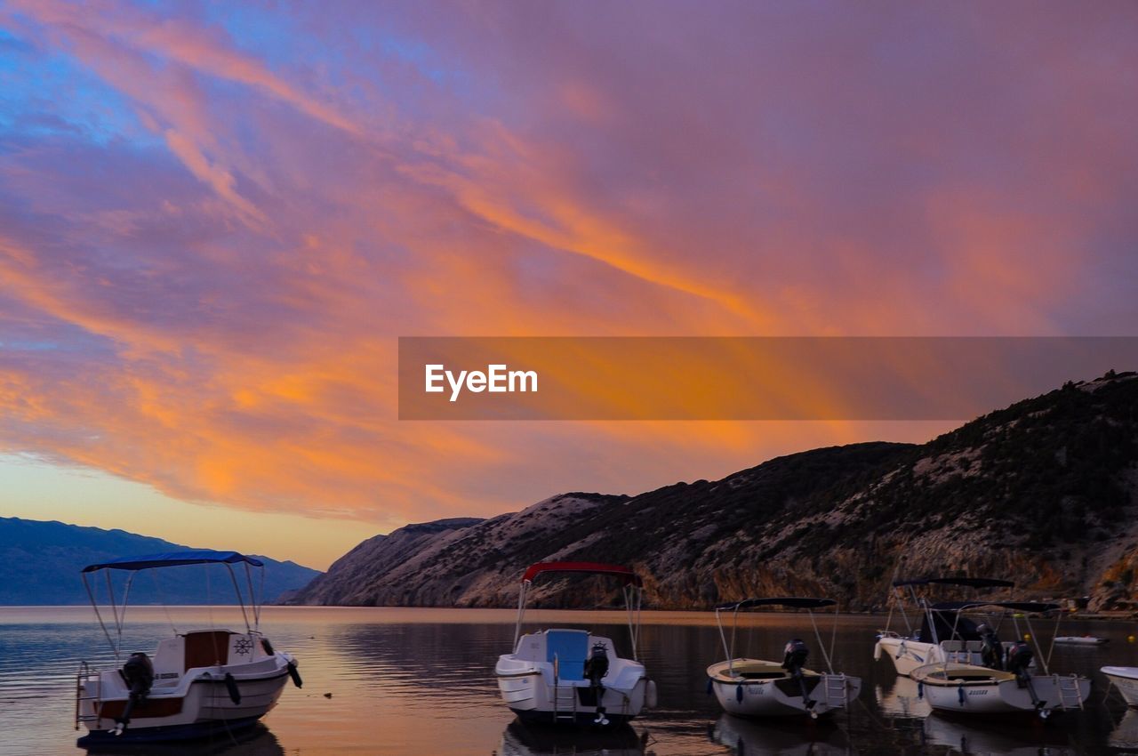 Boats moored on sea against mountains during sunset