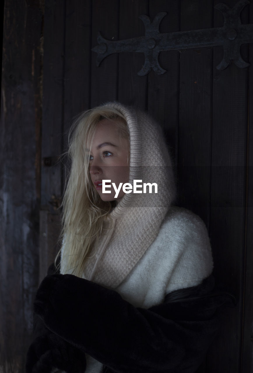 one person, blond hair, darkness, women, portrait, emotion, clothing, looking at camera, adult, child, female, sadness, long hair, fear, black, waist up, hairstyle, dark, young adult, winter, indoors, human face, standing, childhood, spooky, person, door, looking, contemplation, entrance