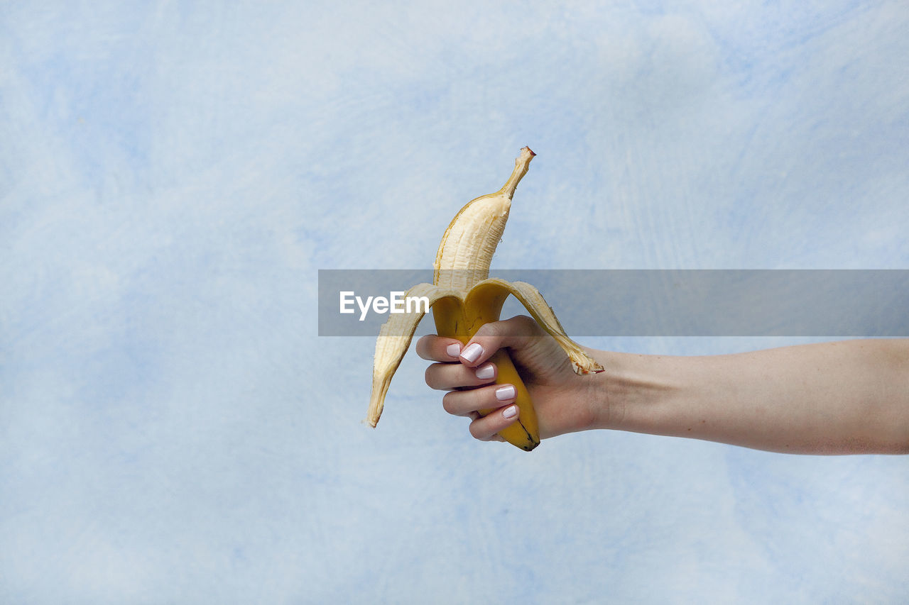 Close-up of woman holding banana against sky