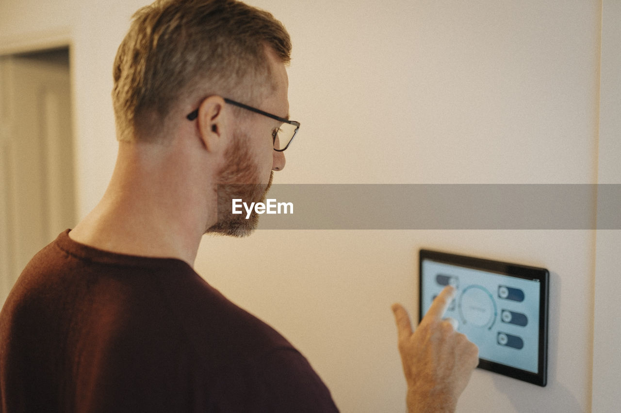 Mature man using digital tablet mounted on wall at smart home