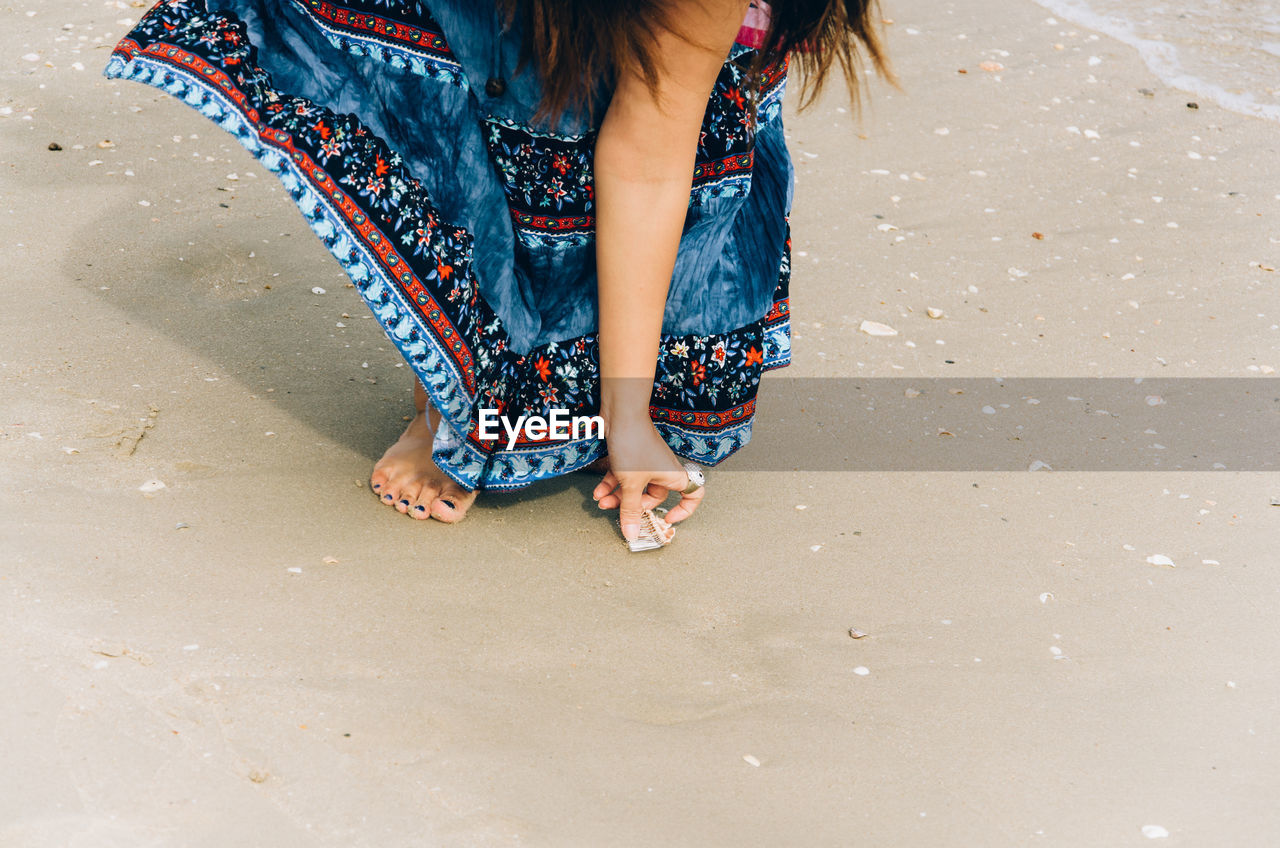 Low section of woman picking seashell at beach