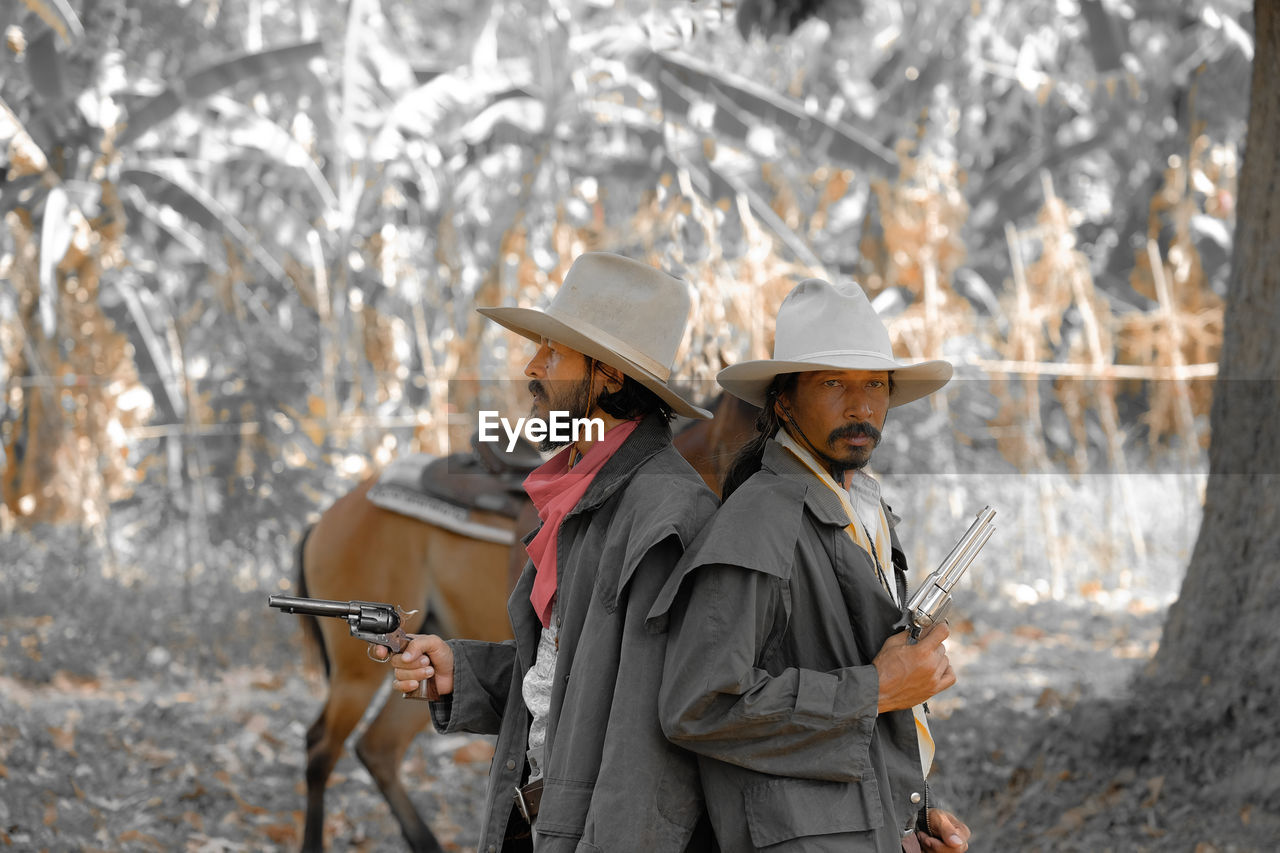 Male friends wearing hats holding guns in forest