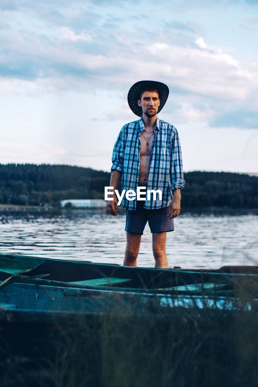 Full length portrait of young man standing in sea against sky