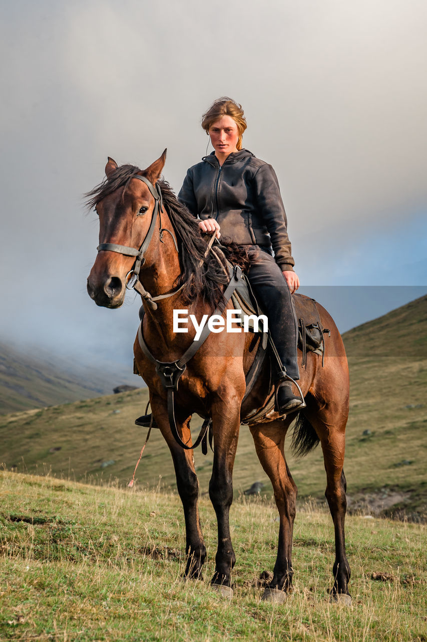 A cowgirl shepherd rider on a horse standing on a mountain valley on autumn day sky with clouds