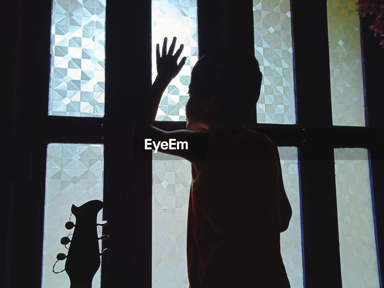 Rear view of silhouette boy standing by window at home