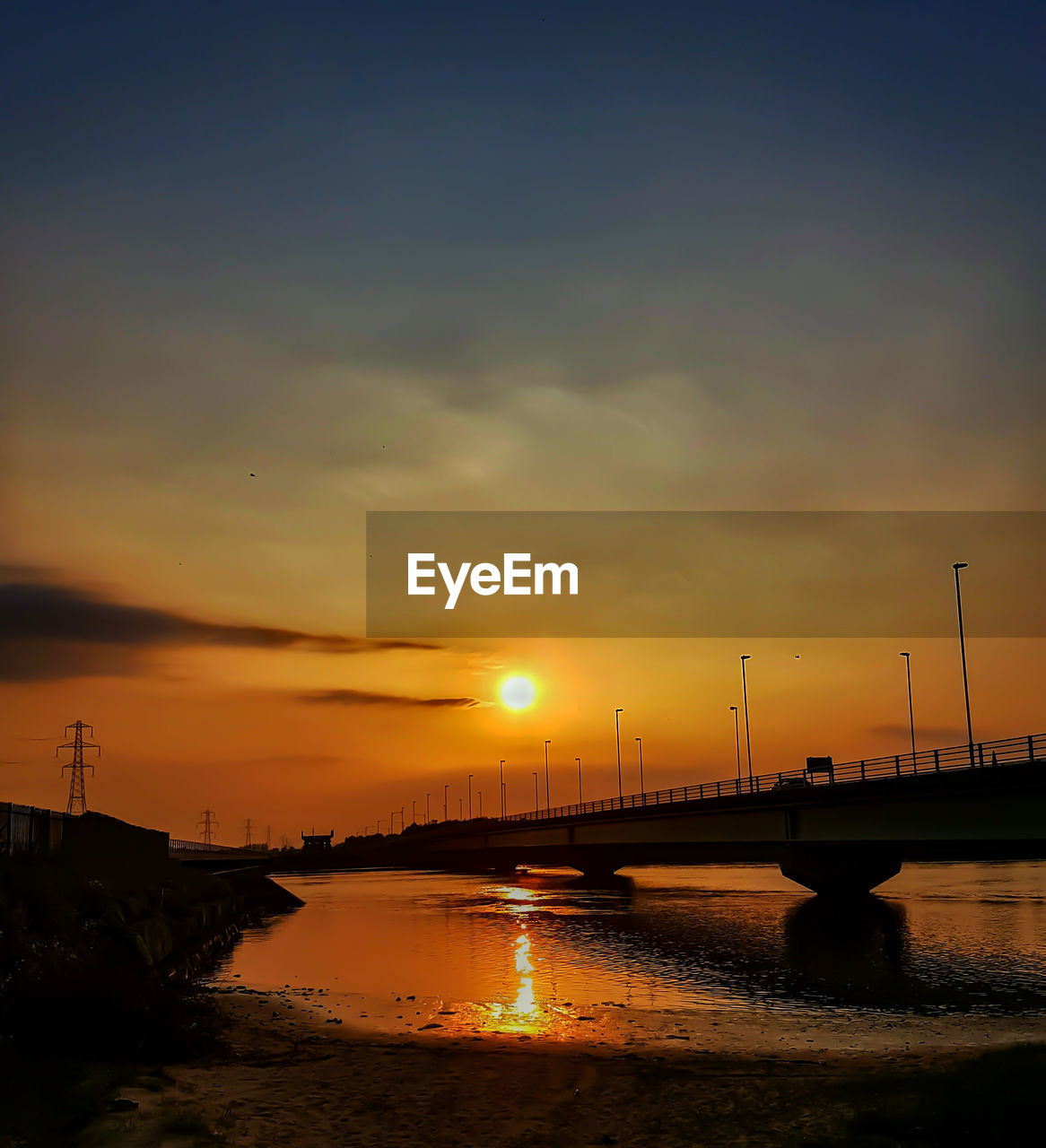 Silhouette bridge over calm river at sunset