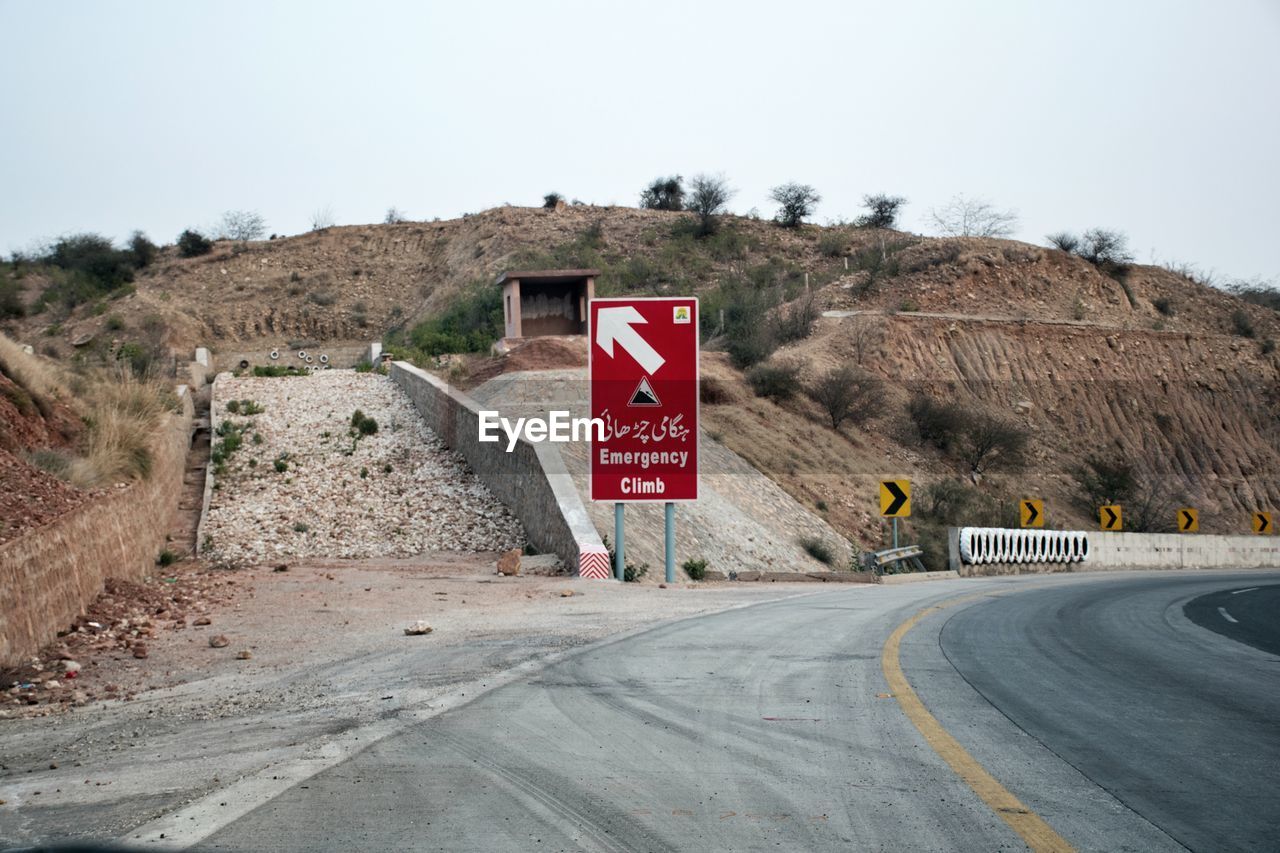 Road sign by highway against sky