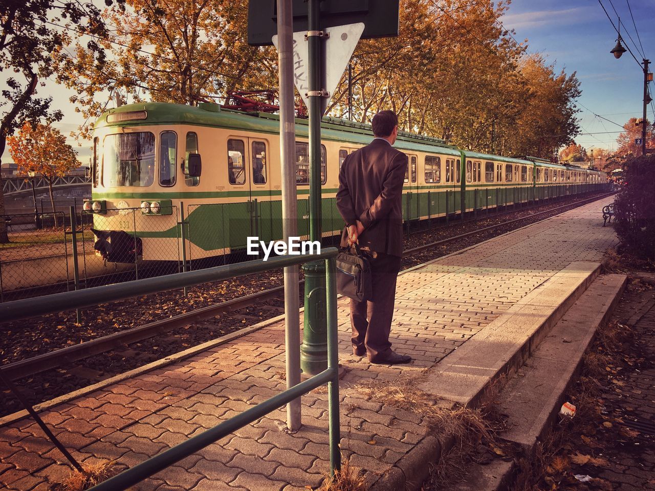 REAR VIEW OF MAN STANDING ON RAILROAD PLATFORM